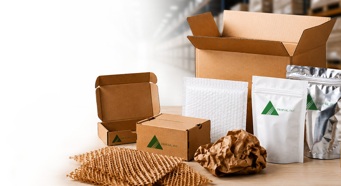 Contact Header Various packaging materials, including cardboard boxes, crumpled paper, a bubble mailer, and silver pouches on a tabletop with a blurred warehouse backdrop.