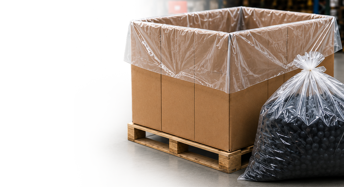 Large cardboard box on a wooden pallet with a clear plastic liner, next to a transparent bag filled with black spheres.