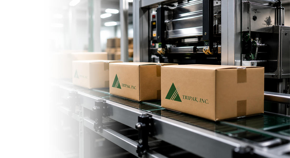 Conveyor belt in a packaging plant with brown boxes labeled Tripak, Inc. moving along.