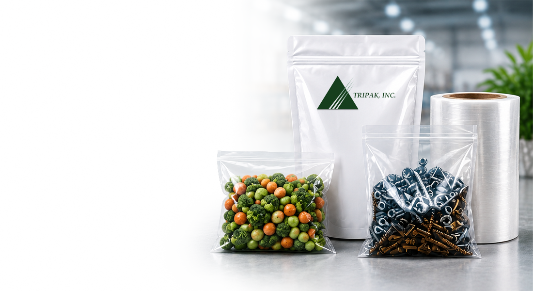 Clear plastic bags filled with mixed vegetables and metal hardware sit on a table. A branded, white stand-up pouch labeled "Tripak, Inc." and a roll of packaging material are in the background, set against a blurred warehouse setting.