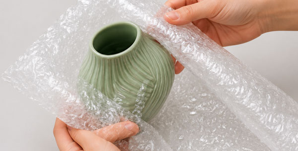 Easy to Use Bubble Wrap Hands unwrapping a light green ribbed vase from bubble wrap.