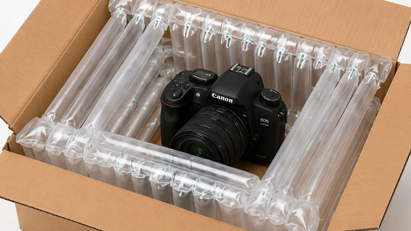 A Canon EOS camera packed in a cardboard box with inflatable air cushions.